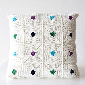 May include: White crocheted pillow with a geometric pattern and colorful accents. The pillow is decorated with small, colorful circles in shades of blue, green, purple, and black.