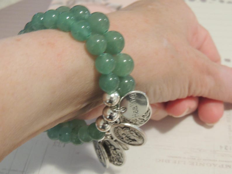 May include: A green jade stone bracelet with silver charms. The charms have the word "healing" engraved on them.