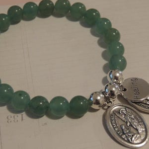 May include: A green jade stone bracelet with silver charms. The charms are engraved with the words "Healing" and "St. Raphael".