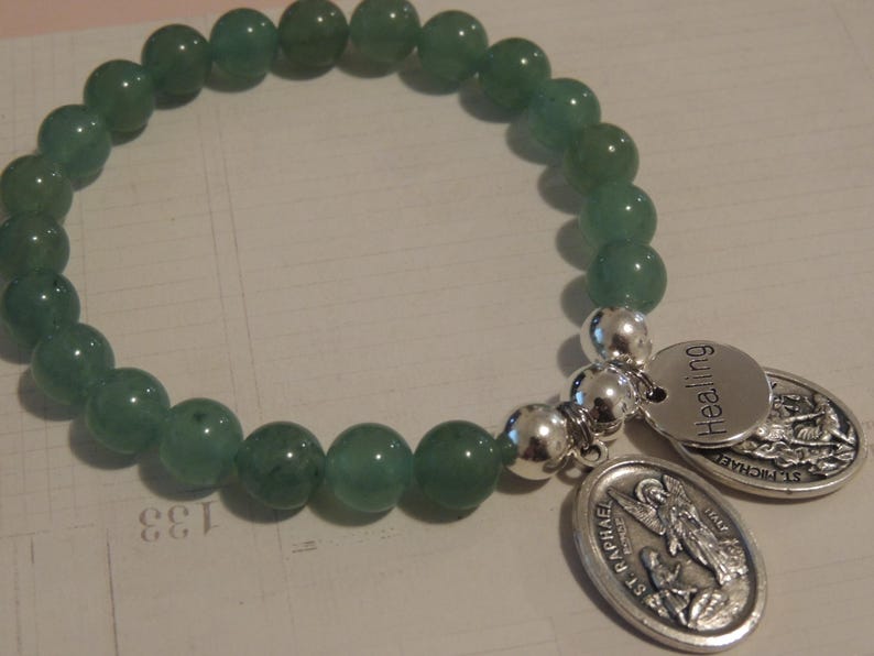 May include: A green jade stone bracelet with silver charms. The charms are engraved with the words "Healing" and "St. Raphael".