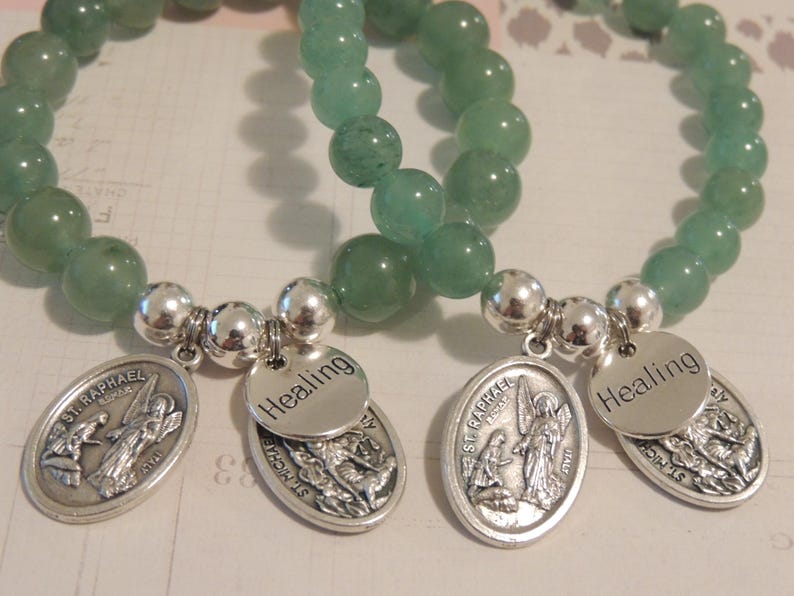 May include: Two green stone beaded bracelets with silver charms. One charm features a depiction of Saint Raphael and the text "Healing". The other charm features a depiction of Saint Michael and the text "Healing".