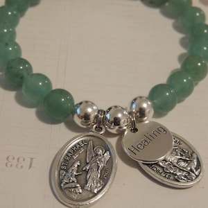May include: A green gemstone bracelet with silver beads and charms. The charms feature the words "Healing" and "St. Raphael" with religious imagery.