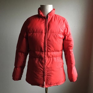 May include: A red puffer jacket with a zipper closure. The jacket is on a mannequin and has a quilted design.