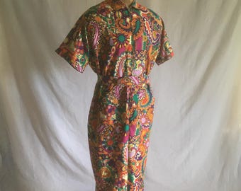 May include: A vintage jumpsuit with a vibrant paisley pattern in shades of orange, green, purple, and pink. The short-sleeved top has a button-down front and a matching belt cinches the waist. The pants are wide-legged.