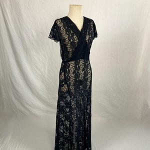 May include: A black lace maxi dress with a V-neckline and short sleeves. The dress is fitted through the bodice and flows out to a full skirt.