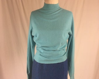 May include: A light blue turtleneck sweater with long sleeves and a dark blue skirt with a checkered pattern.