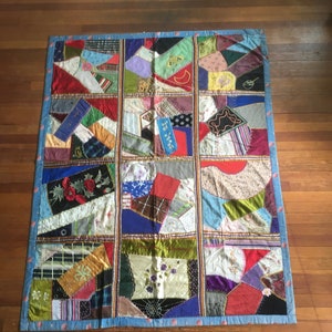 May include: A patchwork quilt with a blue border and a variety of colorful fabrics. The quilt is made up of 16 squares, each with a different pattern. The quilt is made with a variety of fabrics, including silk, velvet, and cotton.