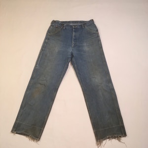 Op de afbeelding: Een paar blauwe spijkerbroeken met een rafelige zoom. De broek heeft een knoopsluiting en vijf zakken.