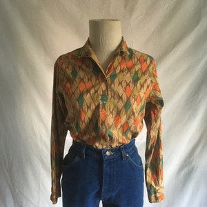 May include: A long-sleeved button-down shirt with a geometric pattern in shades of brown, orange, green, and blue. The shirt is worn over a pair of blue jeans.