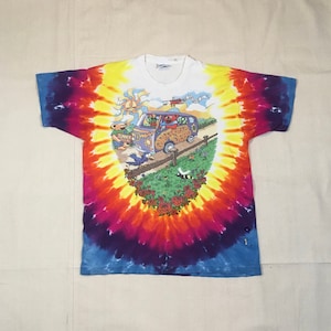 May include: A tie-dye t-shirt with a colorful swirl pattern. The shirt features a cartoon image of a van with the words "Grateful Dead" on the side. The van is surrounded by cartoon characters and flowers.