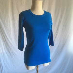 May include: A bright blue, long-sleeved t-shirt with a round neckline. The shirt is on a white mannequin.