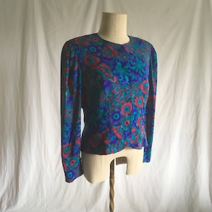 Op de afbeelding: Een blouse met lange mouwen met een levendige bloemenprint in tinten roze, blauw en groen. De blouse heeft een aansluitende pasvorm en een ronde hals.