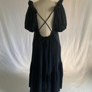 May include: A black maxi dress with a low back and crisscross straps. The dress features short, puffy sleeves and a tiered skirt. The dress is displayed on a mannequin against a white backdrop.
