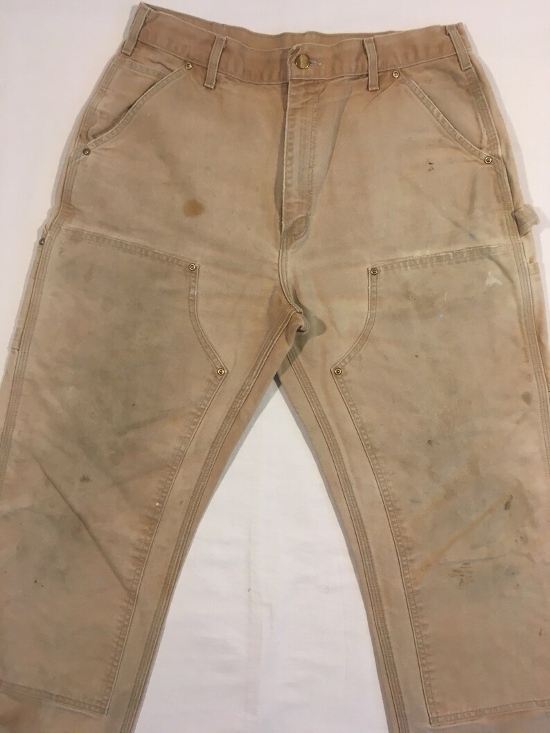 Puede incluir: Un par de pantalones de trabajo de color marr&oacute;n claro con m&uacute;ltiples bolsillos y costuras reforzadas. Los pantalones muestran signos de desgaste, incluyendo manchas y decoloraci&oacute;n.