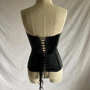 May include: Black satin corset with a lace-up back. The corset is strapless and has a boned structure.