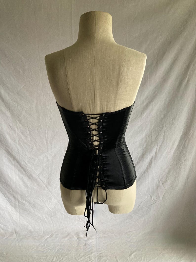 May include: Black satin corset with a lace-up back. The corset is strapless and has a boned structure.