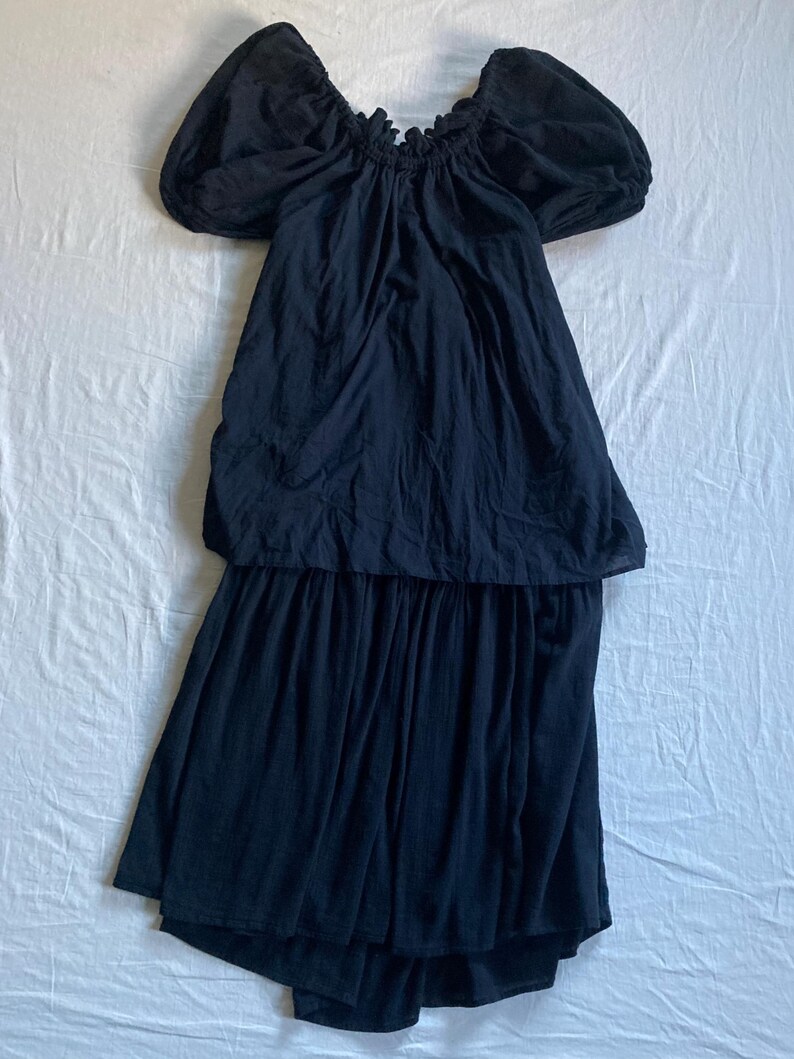 May include: A black dress with an off-the-shoulder neckline and short, puffed sleeves. The dress has a gathered bodice and a tiered skirt, creating a flowing silhouette. The fabric appears to be a lightweight material, suitable for warm weather.