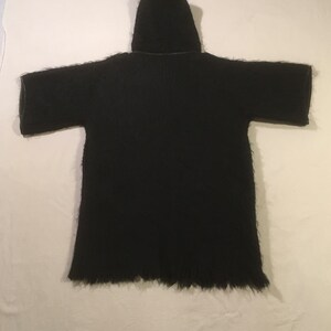 May include: Black hooded cardigan with a long, fringed hem. The cardigan is made of a soft, fuzzy material.