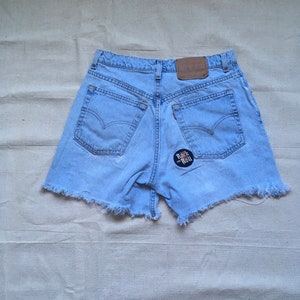Op de afbeelding: Lichtblauwe denim shorts met rafelige randen en een "Rock and Roll" patch op de achterzak.