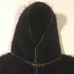 May include: Black hooded cape with a leather trim and a gold clasp.