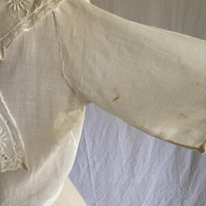 May include: Off-white vintage blouse with a detailed embroidered collar and sleeve. The collar features delicate floral embroidery and lace trim. The sleeve shows some discoloration. The blouse is made of a lightweight fabric.