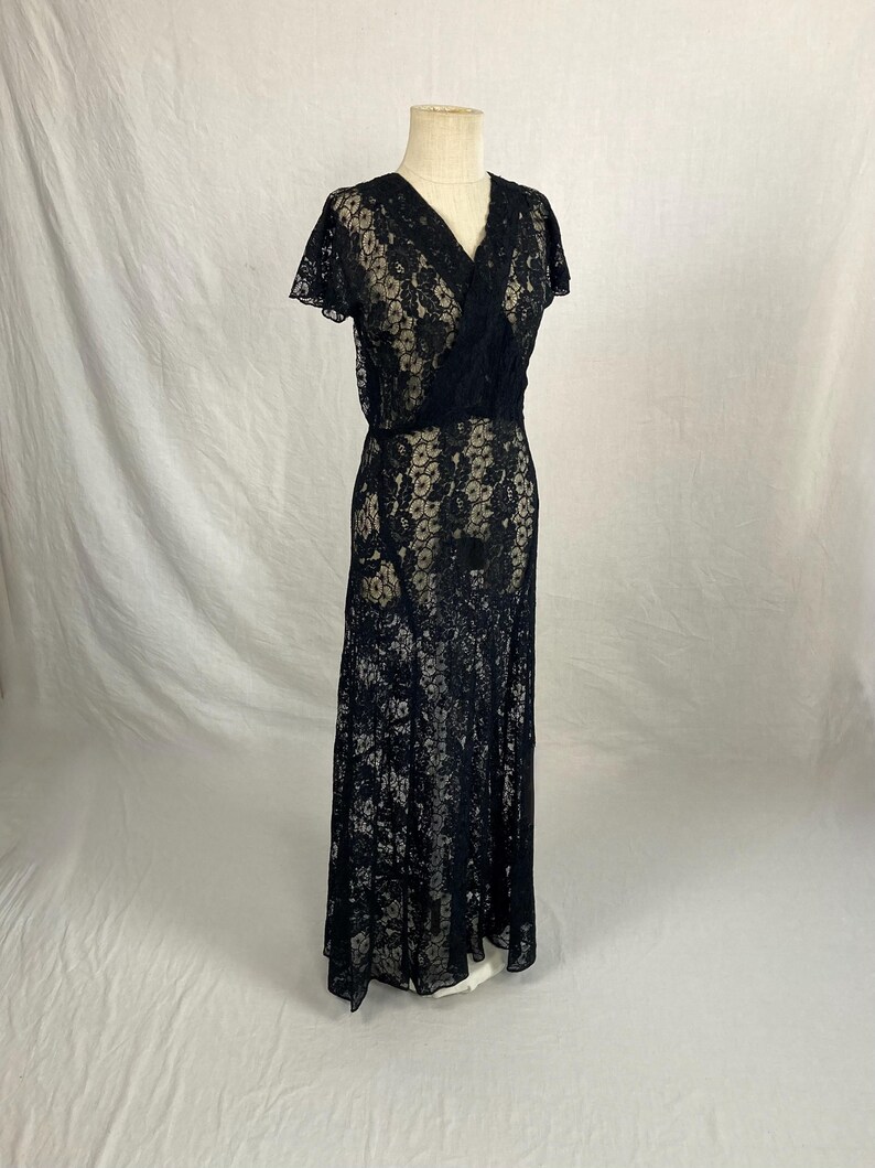 May include: A black lace maxi dress with a V-neckline and short sleeves. The dress is fitted through the bodice and flows out to a full skirt.