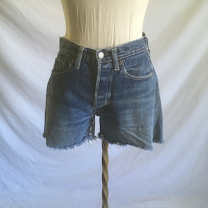 Puede incluir: Un par de pantalones cortos de mezclilla azul con dobladillo deshilachado. Los pantalones cortos tienen cierre de botón y cinco bolsillos.