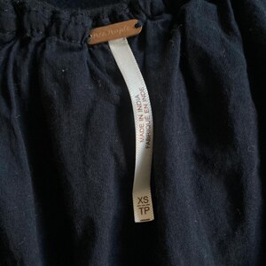 May include: Close-up of a dark navy blue garment with a tag that reads "Free People." A white tag with the text "MADE IN INDIA FABRIQUE EN INDE" and size "XS TP" is attached to the garment.