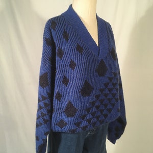 May include: A blue and black patterned sweater with a v-neck. The sweater is knitted and has a geometric design.