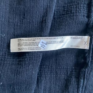 May include: Close-up of a dark blue fabric with a textured pattern. A white tag is attached, displaying washing instructions and a product code. The tag includes text in English and French.