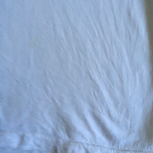 May include: White t-shirt with a smooth, slightly wrinkled texture. The shirt has a hemmed edge.