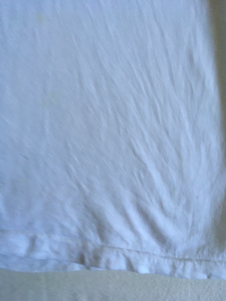 May include: White t-shirt with a smooth, slightly wrinkled texture. The shirt has a hemmed edge.