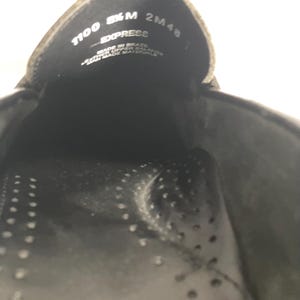May include: Close-up of the inside of a black shoe. The shoe's interior features a perforated insole and the text "1100 8&frac12; M EXPRESS 2M48". The shoe is made in Brazil with leather upper and man-made materials.