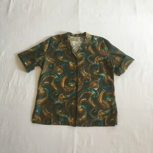 May include: A short-sleeved shirt with a green and gold swirling pattern. The shirt has a button-up front and a collar.