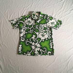 May include: A green and white short-sleeved shirt with a floral print. The shirt has a button-up front and a collar.