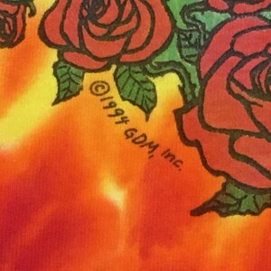 May include: A tie-dye t-shirt with a red, yellow, and orange color scheme. The shirt features a black and white graphic of roses with green leaves. The text "&copy;1994 60M, Inc." is printed on the shirt.