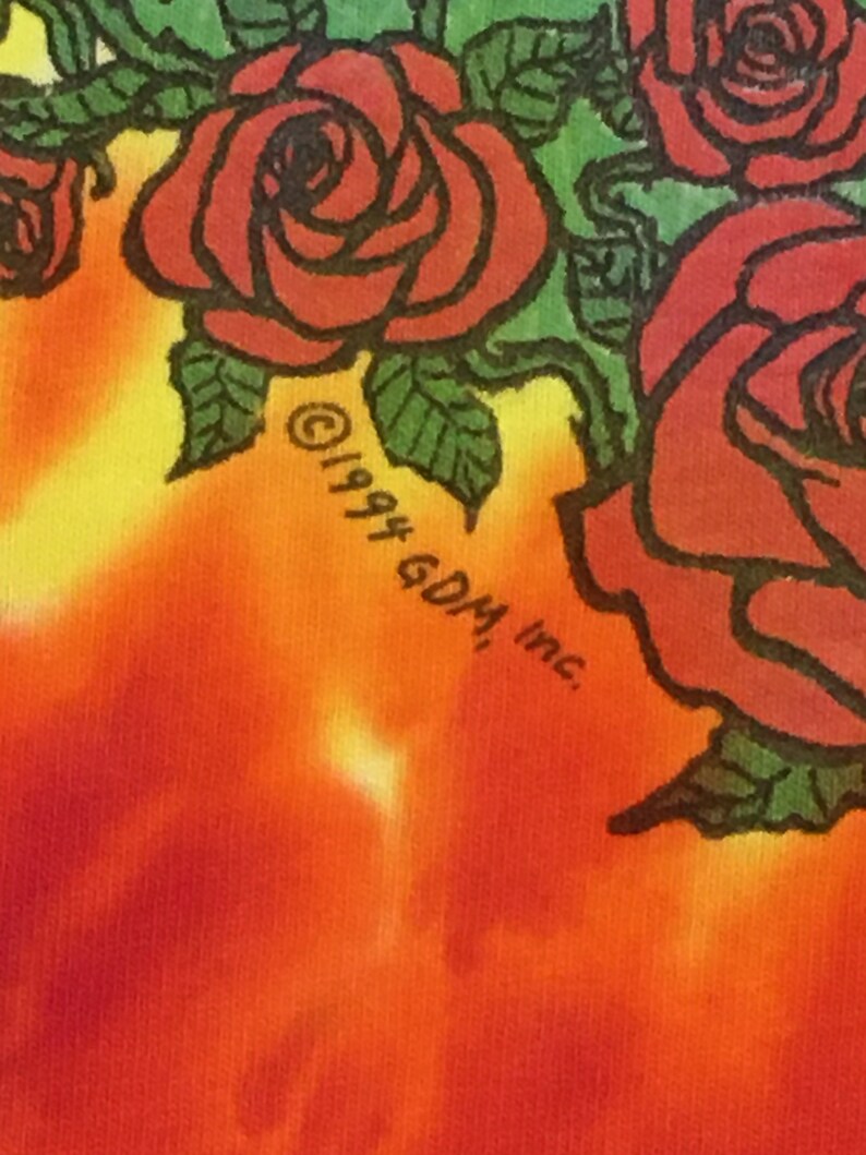 May include: A tie-dye t-shirt with a red, yellow, and orange color scheme. The shirt features a black and white graphic of roses with green leaves. The text "&copy;1994 60M, Inc." is printed on the shirt.