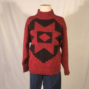 Puede incluir: Suéter rojo con un patrón geométrico negro. El suéter tiene cuello alto y mangas largas.