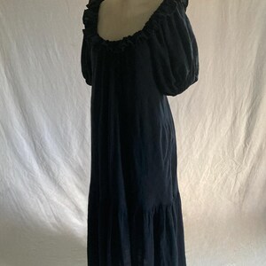 May include: A dark navy blue maxi dress displayed on a mannequin. The dress features a ruffled neckline, short puffed sleeves, and a tiered skirt. The fabric appears to be a lightweight material, suitable for warmer weather. The dress is floor-length.