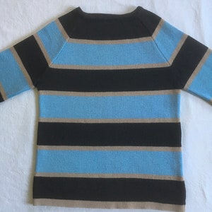 May include: A striped sweater with black, light blue, and beige stripes. The sweater has a crew neck and long sleeves.