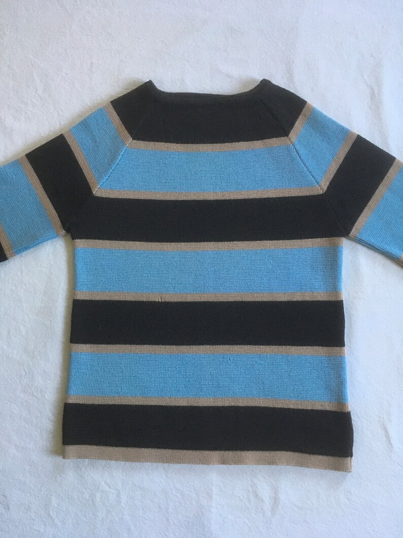 May include: A striped sweater with black, light blue, and beige stripes. The sweater has a crew neck and long sleeves.