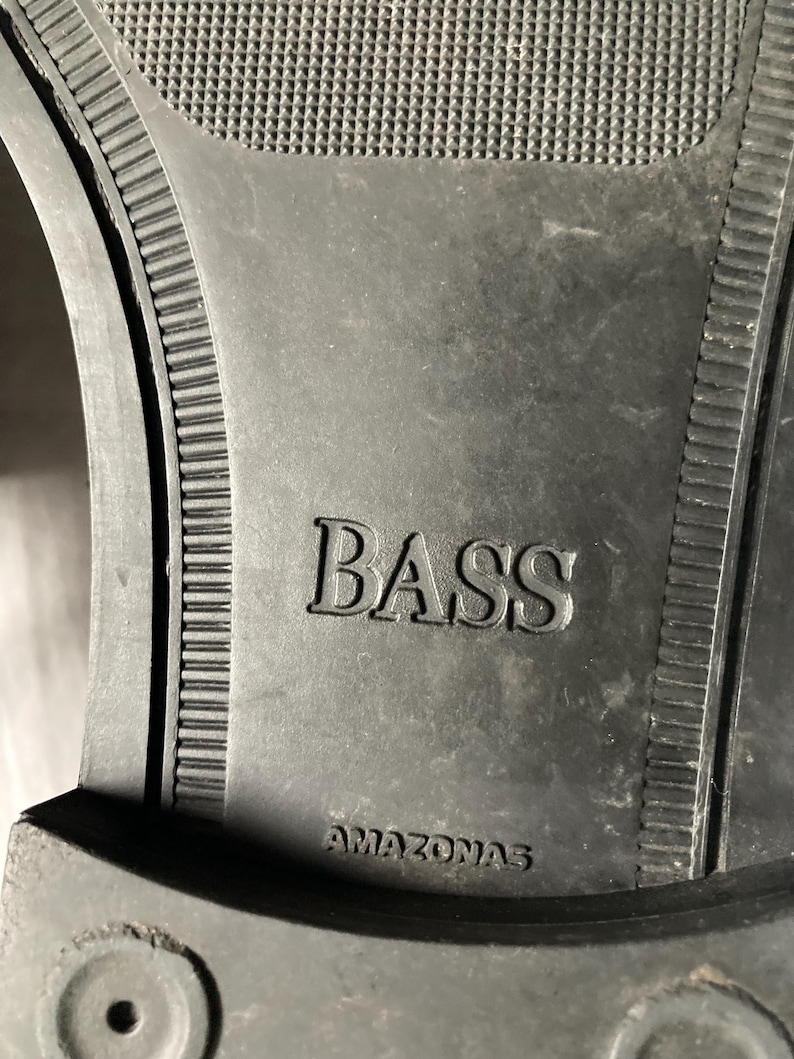 May include: Close-up of a black shoe sole with the embossed word "BASS" and the word "AMAZONAS" underneath. The sole has a textured pattern and a ridged border.