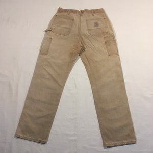 Puede incluir: Un par de pantalones de trabajo de mezclilla beige con un parche marr&oacute;n en el bolsillo trasero derecho.