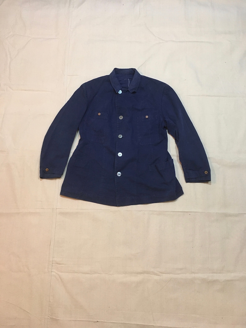 May include: A dark blue work jacket with a button-up front and multiple pockets. The jacket has a collar and long sleeves.