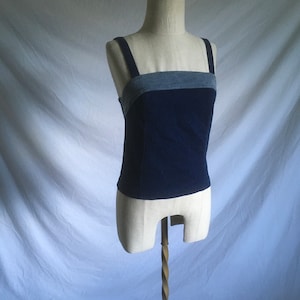 May include: A navy blue sleeveless top with a light blue band across the chest. The top is on a white mannequin.
