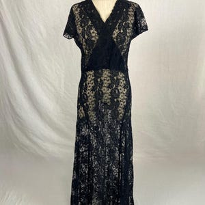 May include: A black lace dress with a V-neckline and short sleeves. The dress is floor-length and has a fitted bodice and a flowing skirt.