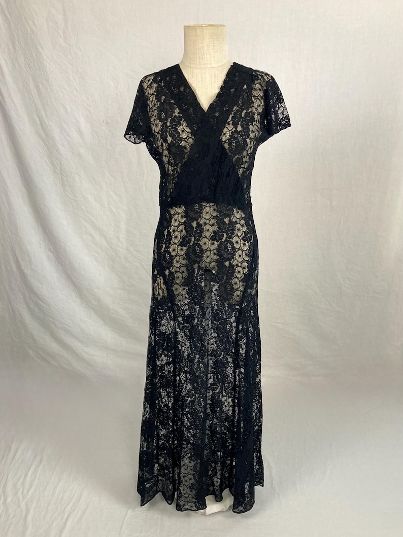 May include: A black lace dress with a V-neckline and short sleeves. The dress is floor-length and has a fitted bodice and a flowing skirt.