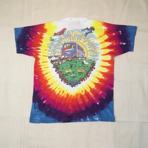 May include: Tie-dye t-shirt with a colorful swirl pattern. The shirt features a graphic of a psychedelic bus with the text "Summer Tour 1994" on the front.
