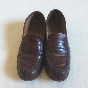 May include: A pair of brown leather loafers with a penny strap detail. The loafers have a rounded toe and a stitched edge.