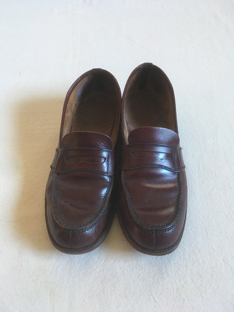 May include: A pair of brown leather loafers with a penny strap detail. The loafers have a rounded toe and a stitched edge.